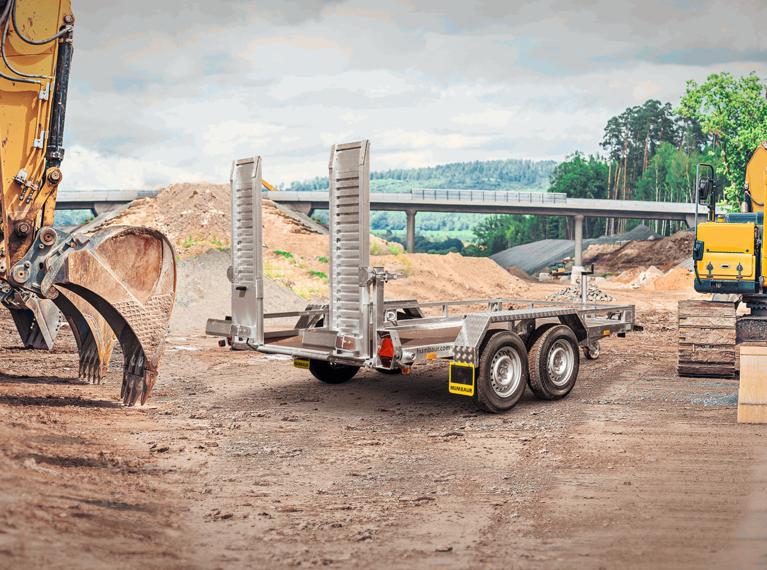 HS Basis, Ein Humbaur Baumaschienen Transporter mit Auffahrbohlen der auf einer Baustelle steht, Rechts vorne | © Humbaur GmbH