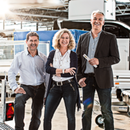 Eine Frau und zwei Männer stehen in der Werkshalle vor einer Auswahl verschiedener Humbaur Anhänger. | © Humbaur GmbH