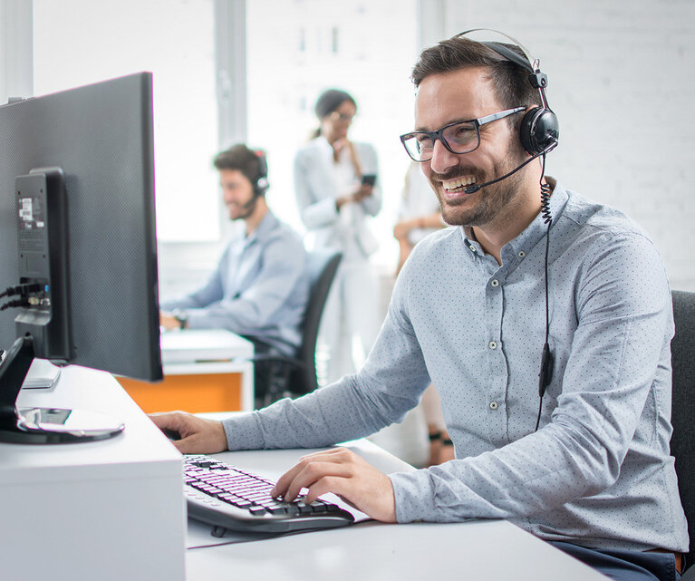 Mitarbeiter arbeitet an einem Computer mit Headset und lächelt | © Humbaur GmbH