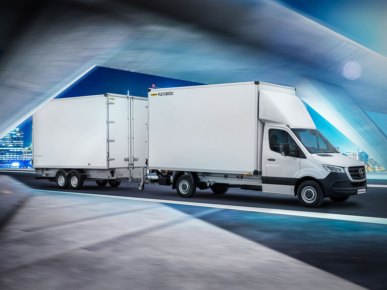 Humbaur Durchladezug bestehend aus einem Fahrzeug mit Flexbox-Aufbau und einem Kofferanhänger fährt auf einer beleuchteten Straße.  | © Humbaur GmbH